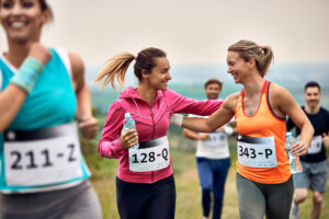 carrera con causa benéfica donde hay 3 mujeres y dos se están ayudando, en el fondo hay dos hombre corriendo, campo y montañas